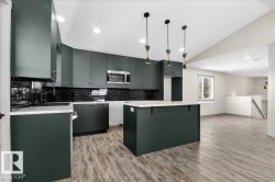 Modern kitchen featuring deep green cabinetry with black hardware, white countertops, and a black subway tile backsplash - 