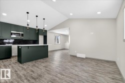 Open-concept kitchen featuring dark green cabinetry, a black subway tile backsplash, and a central island with a light-toned countertop - 