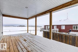 Covered wood-finish deck featuring recessed lighting, a slatted wood railing, and a vinyl soffit ceiling - 