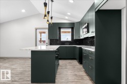 Vaulted ceiling kitchen featuring dark green cabinetry, a central island with a white countertop, and a black subway tile backsplash - 