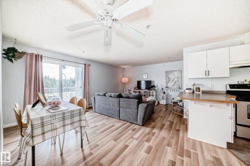 The living area features hardwood floors, a ceiling fan, and a sliding glass door that opens to a balcony with views of trees - 317 7511 171 Street, Edmonton, AB - Indoor