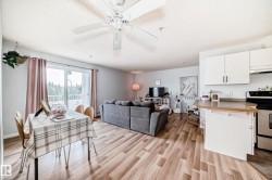 The living area features hardwood floors, a ceiling fan, and a sliding glass door that opens to a balcony with views of trees - 