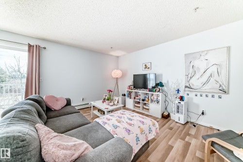 The living space features light-toned flooring, white walls, and a glass-paned sliding door providing access to a balcony with white railings - 317 7511 171 Street, Edmonton, AB - Indoor Photo Showing Living Room
