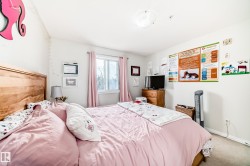 A spacious room featuring a light-colored wood headboard, a window with pink curtains, and light-colored carpeting - 