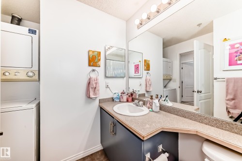 The bathroom features a vanity with a countertop and a white sink, a mirror with overhead lighting, and a stacked washer and dryer - 317 7511 171 Street, Edmonton, AB - Indoor