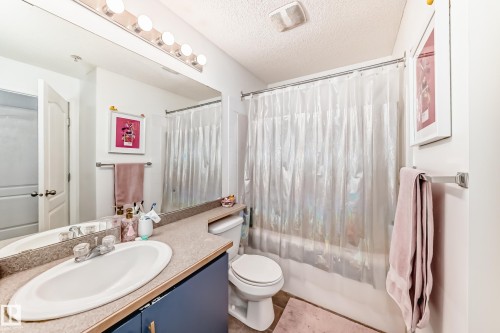 This bathroom features a vanity with a large mirror and overhead lighting, a toilet, and a shower with a clear curtain - 317 7511 171 Street, Edmonton, AB - Indoor Photo Showing Bathroom