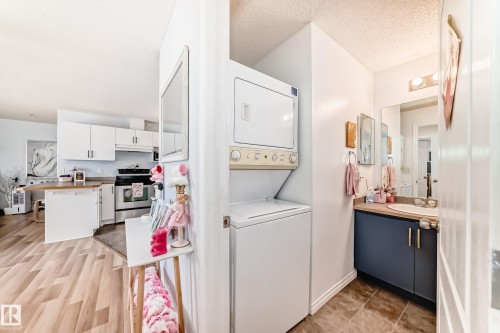 The property features a kitchen with white cabinetry and stainless steel appliances, visible from an area with light-toned flooring - 317 7511 171 Street, Edmonton, AB - Indoor Photo Showing Laundry Room