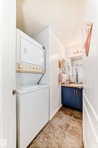 This space includes a stacked washer and dryer, a vanity with a dark blue cabinet, a sink, and a mirror - 317 7511 171 Street, Edmonton, AB - Indoor Photo Showing Laundry Room