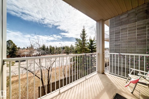 The property features a private balcony with a concrete floor and a white metal railing, offering views of the surrounding trees and the sky - 317 7511 171 Street, Edmonton, AB - Outdoor With Balcony With Exterior