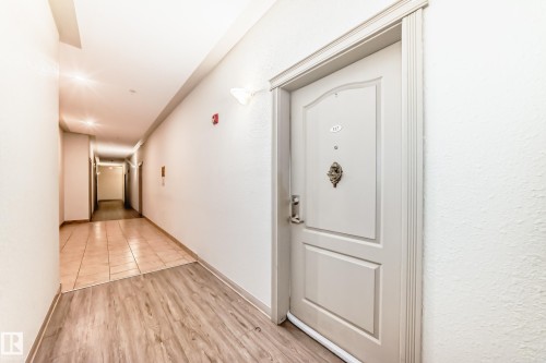 Entrance door featuring a decorative knocker and a light-colored finish, with wood-style flooring at the entryway - 317 7511 171 Street, Edmonton, AB - Indoor Photo Showing Other Room