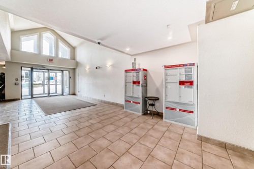The property entrance features automatic glass doors, a high vaulted ceiling, and ample natural light from the large windows above the entrance - 317 7511 171 Street, Edmonton, AB - Indoor Photo Showing Other Room