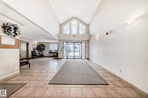 The property features a spacious entryway with tiled flooring and a high vaulted ceiling, complemented by large windows providing natural light - 317 7511 171 Street, Edmonton, AB - Indoor Photo Showing Other Room
