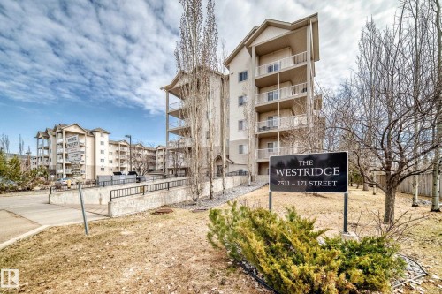 The property features a multi-story building with balconies, set among trees and shrubbery - 317 7511 171 Street, Edmonton, AB - Outdoor With Balcony