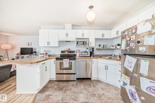 The kitchen features white cabinetry, stainless steel appliances, and a light-toned countertop - 317 7511 171 Street, Edmonton, AB - Indoor Photo Showing Kitchen With Double Sink