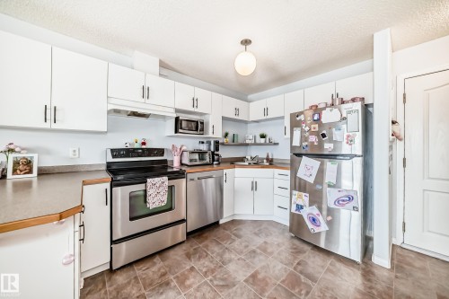 The kitchen features white cabinetry, stainless steel appliances, a corner sink, and tiled flooring - 317 7511 171 Street, Edmonton, AB - Indoor Photo Showing Kitchen With Double Sink