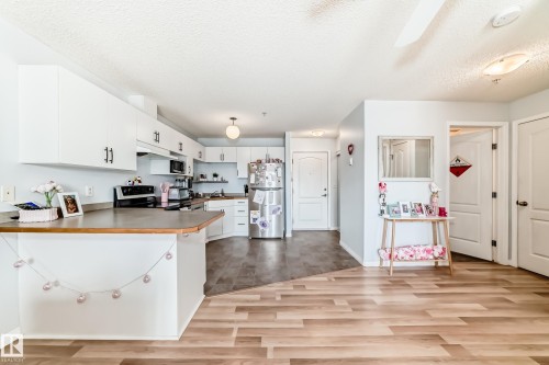 The kitchen features white cabinetry with dark hardware and a stainless steel refrigerator - 317 7511 171 Street, Edmonton, AB - Indoor Photo Showing Kitchen