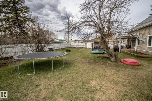 Expansive backyard featuring a partial white picket fence, mature trees, and a visible portion of the home's exterior siding - 5213 49 Ave, St. Paul Town, AB - Outdoor