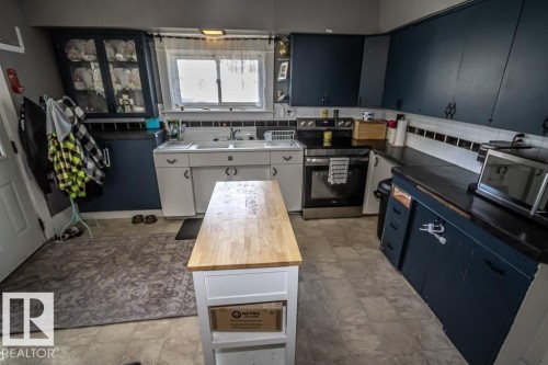 Kitchen featuring a wood-top island, a stainless steel range, and dark cabinetry - 5213 49 Ave, St. Paul Town, AB - Indoor Photo Showing Kitchen
