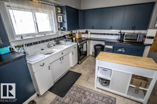 Kitchen featuring dark blue cabinetry, white base cabinets, a double basin sink, black countertops, and light-toned flooring - 5213 49 Ave, St. Paul Town, AB - Indoor Photo Showing Kitchen With Double Sink