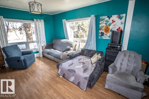 Room featuring wood-finish flooring, two large windows, a ceiling-mounted light fixture, and vibrant wall coloring - 5213 49 Ave, St. Paul Town, AB - Indoor Photo Showing Living Room
