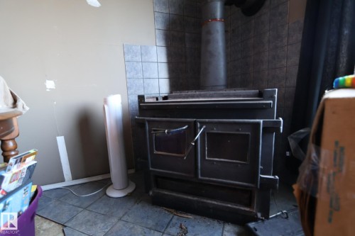 Freestanding wood-burning stove with a metal flue, set against a tiled wall - 4114 Main Street, Ashmont, AB - Indoor