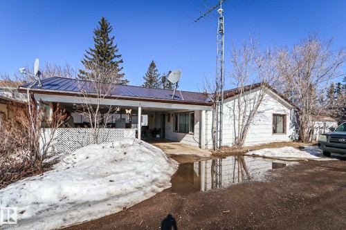 White siding exterior featuring a blue metal roof, covered porch, and mature trees - 4114 Main Street, Ashmont, AB - Outdoor