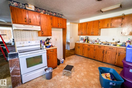 Kitchen featuring a white electric range, integrated range hood, wood cabinetry with dark hardware, and patterned vinyl flooring - 4114 Main Street, Ashmont, AB - Indoor Photo Showing Kitchen With Double Sink