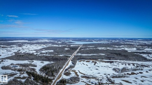 Expansive aerial showcasing a vast winter landscape with a prominent road carving through snow-covered fields and dense tree lines - Sw-34-59-12-4, Spedden, AB 