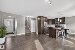 Spacious living area featuring wood-finish flooring, a kitchen island with pendant lighting, stainless steel appliances, and dark wood cabinetry - 