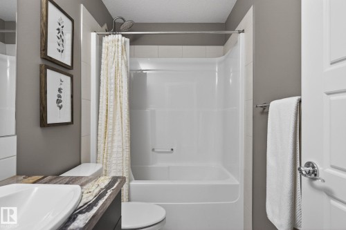 Bathroom featuring a white shower-over-tub unit with subway tile surround, a built-in toilet, a vanity with a surface-mounted rectangular sink, and a multi-toned countertop - 2017 Westerra Loop, Stony Plain, AB - Indoor Photo Showing Bathroom