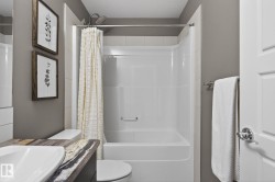 Bathroom featuring a white shower-over-tub unit with subway tile surround, a built-in toilet, a vanity with a surface-mounted rectangular sink, and a multi-toned countertop - 