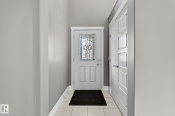 Entryway featuring a white door with decorative glass inserts, white trim, light gray walls, and light-toned tile flooring - 
