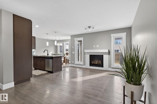Open-concept living area with wood-finish flooring, a contemporary fireplace featuring a white mantle, and large windows - 2017 Westerra Loop, Stony Plain, AB - Indoor With Fireplace
