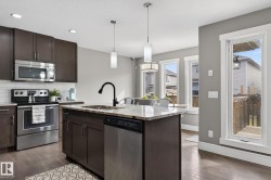 Modern kitchen featuring dark wood cabinetry, stainless steel appliances, granite countertops, an island with an undermount sink and black faucet, and pendant lighting - 