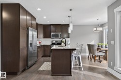Kitchen featuring dark wood-finish cabinetry, stainless steel appliances, a light-colored countertop on the island, a subway tile backsplash, and recessed lighting - 