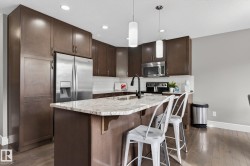 Kitchen featuring a central island with a light-toned countertop, dark wood cabinetry, a stainless steel refrigerator, and a tile backsplash - 