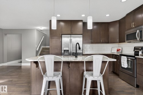 Kitchen island featuring a granite-style countertop, undermount sink with a matte black faucet, and two contemporary pendant lights - 2017 Westerra Loop, Stony Plain, AB - Indoor Photo Showing Kitchen With Upgraded Kitchen