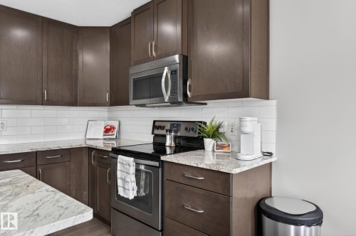 Modern kitchen featuring dark wood-finish cabinetry, light speckled countertops, a white subway tile backsplash, and stainless steel appliances including a microwave and range - 2017 Westerra Loop, Stony Plain, AB - Indoor Photo Showing Kitchen With Upgraded Kitchen