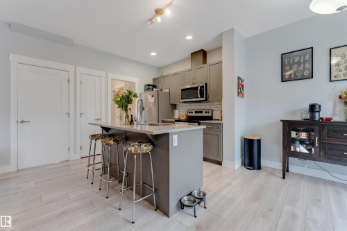 Open concept kitchen featuring an island with countertop seating, stainless steel appliances, grey cabinetry, and a white subway tile backsplash - 11 4835 Wright Drive, Edmonton, AB - Indoor Photo Showing Kitchen