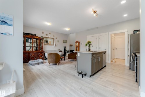 Open-concept living space featuring light wood-finish flooring, recessed lighting, and a kitchen island with integrated sink and seating - 11 4835 Wright Drive, Edmonton, AB - Indoor Photo Showing Other Room