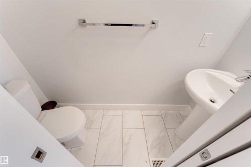 Pedestal sink with chrome faucet, toilet, and light-toned tile flooring - 11 4835 Wright Drive, Edmonton, AB - Indoor Photo Showing Bathroom