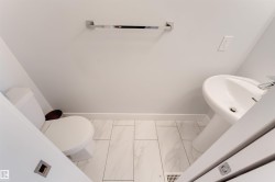Pedestal sink with chrome faucet, toilet, and light-toned tile flooring - 