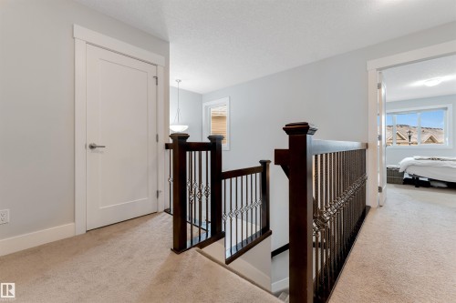 Upper-level hallway featuring a dark wood staircase railing with decorative metal spindles - 11 4835 Wright Drive, Edmonton, AB - Indoor