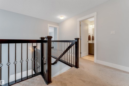 Upper hallway with dark wood railing featuring ornate iron balusters, light gray walls, and neutral carpet - 11 4835 Wright Drive, Edmonton, AB - Indoor Photo Showing Other Room