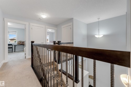 Upper-level hallway featuring plush carpeting, white trim, and a dark wood and wrought iron staircase railing - 11 4835 Wright Drive, Edmonton, AB - Indoor Photo Showing Other Room