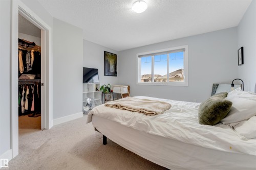 Bedroom featuring plush carpeting, a large window, neutral wall tones, white trim, and a built-in closet with shelving and hanging rods - 11 4835 Wright Drive, Edmonton, AB - Indoor Photo Showing Bedroom