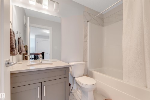 Bathroom featuring a gray vanity with an integrated sink, polished chrome faucet, stone-finish countertop, and a full-width mirror - 11 4835 Wright Drive, Edmonton, AB - Indoor Photo Showing Bathroom