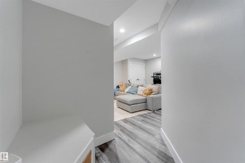 Hallway with light gray walls, white trim, and wood-finish flooring leading to a living area with recessed lighting - 11 4835 Wright Drive, Edmonton, AB - Indoor Photo Showing Other Room