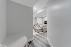 Hallway with light gray walls, white trim, and wood-finish flooring leading to a living area with recessed lighting - 