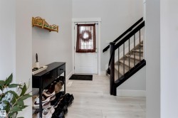 Entryway featuring light wood-finish flooring, a white door with dark trim, and a carpeted staircase with dark wood and wrought iron balusters - 